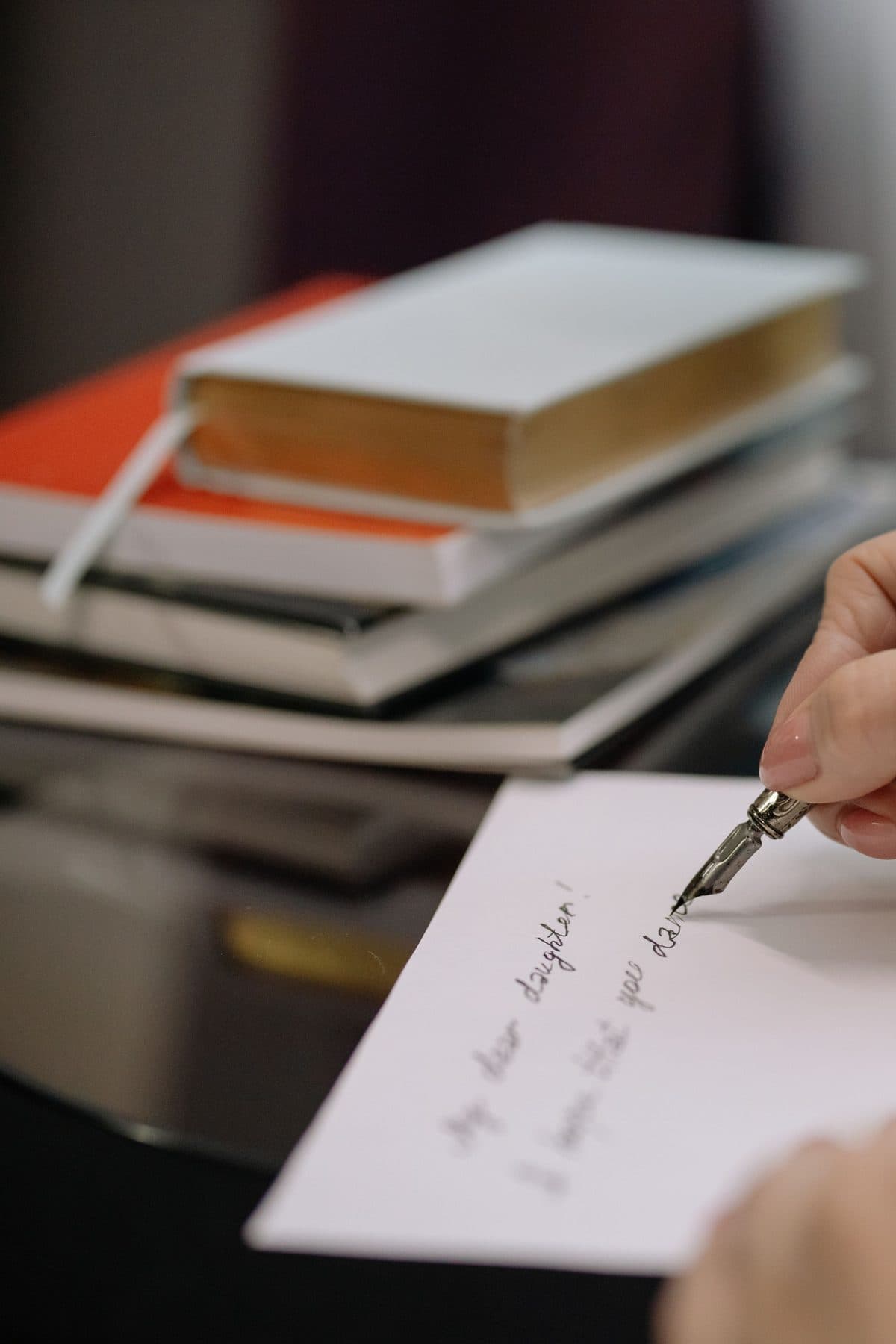 Iemand schrijft met een vulpen een brief, naast een stapel boeken